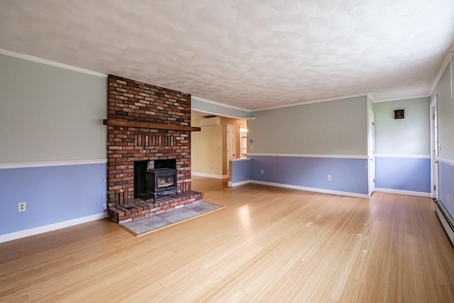 704 Brighton Hill Rd, Minot, ME 04258 - unfurnished living room with a wall mounted AC, wood finished floors, a wood stove, a textured ceiling, and crown molding