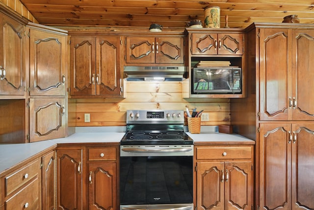 23 Mccutcheon Way, Sidney, ME 04330 - kitchen with under cabinet range hood, stainless steel range with electric stovetop, black microwave, light countertops, and wooden walls