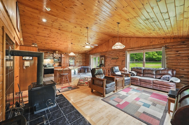 23 Mccutcheon Way, Sidney, ME 04330 - living area featuring plenty of natural light, rustic walls, wood ceiling, a wood stove, and ceiling fan