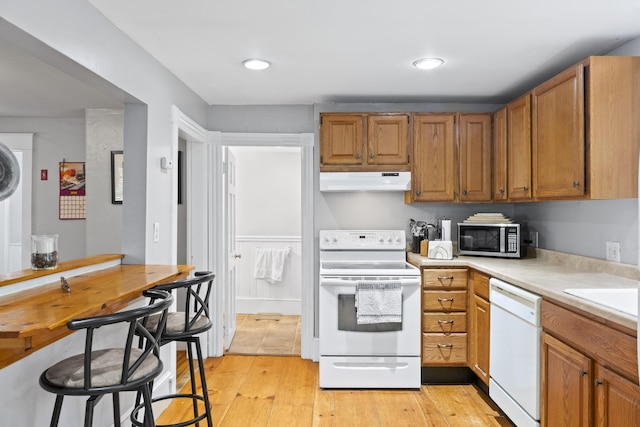 68 Newbury St, Auburn, ME 04210 - kitchen with white appliances, under cabinet range hood, light countertops, light wood-style flooring, and brown cabinetry