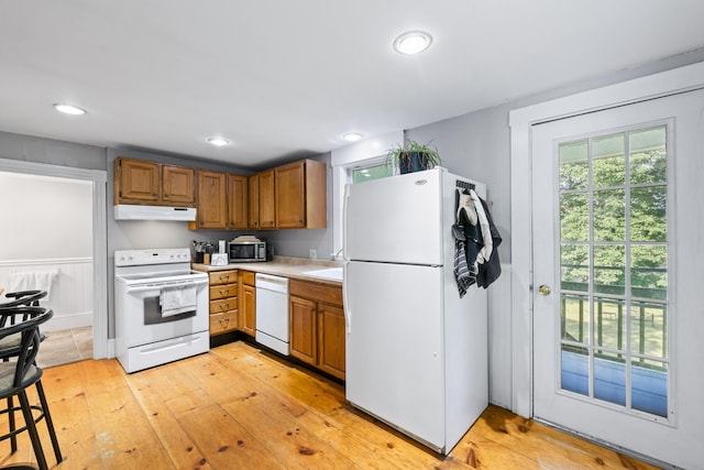 68 Newbury St, Auburn, ME 04210 - kitchen with white appliances, under cabinet range hood, light wood-style flooring, light countertops, and brown cabinets