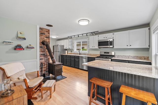 23 Cottage Dr, Friendship, ME 04547 - kitchen featuring appliances with stainless steel finishes, a wood stove, a kitchen breakfast bar, light wood-style floors, and white cabinetry