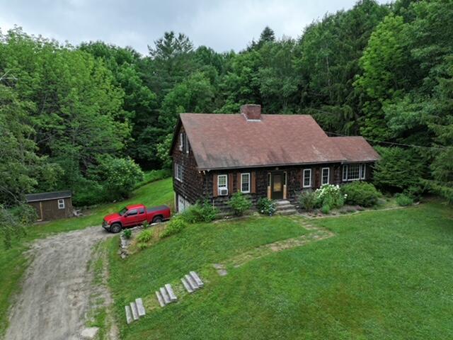 32 Williams Rd, Chelsea, ME 04330 - view of front of house featuring a chimney, a forest view, a front lawn, dirt driveway, and a storage shed