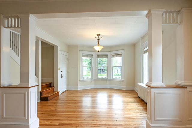 18 Colonial Rd Unit 18, Portland, ME 04102 - unfurnished dining area featuring light wood finished floors, stairs, radiator heating unit, decorative columns, and ornamental molding