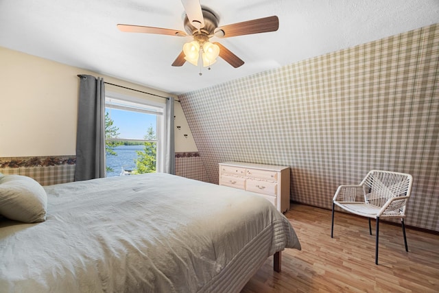 52 Ludden Ln, Lincoln, ME 04457 - bedroom with wallpapered walls, wood finished floors, an accent wall, a wainscoted wall, and a water view