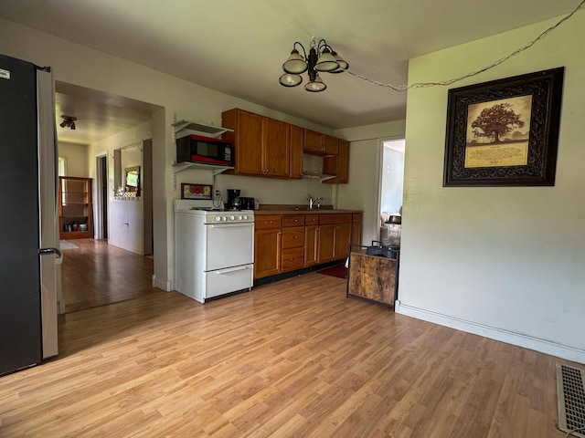 27 Main St, Vassalboro, ME 04989 - kitchen with white range with gas stovetop, black microwave, freestanding refrigerator, a chandelier, and brown cabinetry