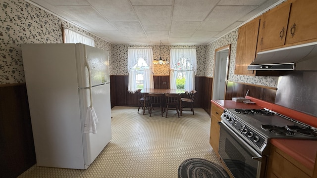 269 County Rd, Lubec, ME 04652 - kitchen featuring wallpapered walls, gas range oven, wainscoting, freestanding refrigerator, and under cabinet range hood