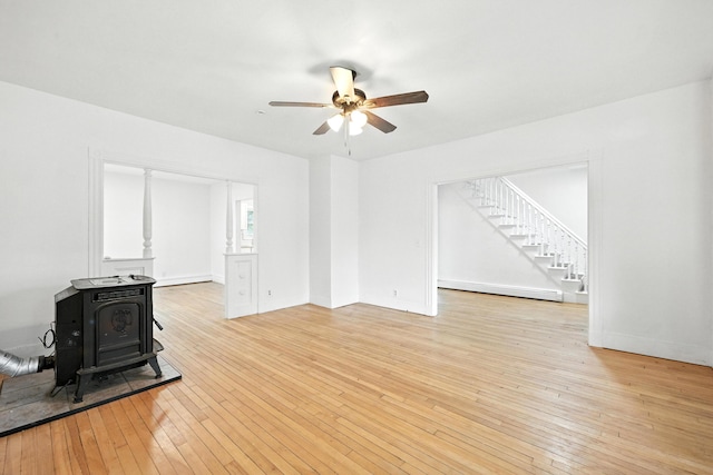38 Silvermount St, Waterville, ME 04901 - unfurnished living room featuring a wood stove, a baseboard heating unit, ceiling fan, light wood-style flooring, and stairs