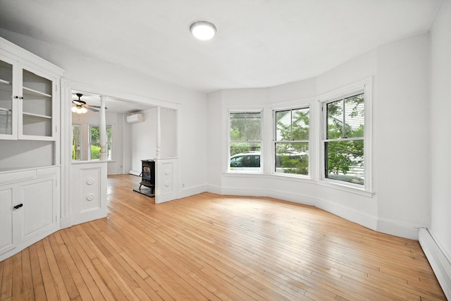 38 Silvermount St, Waterville, ME 04901 - unfurnished living room featuring a wood stove, baseboard heating, plenty of natural light, and an AC wall unit