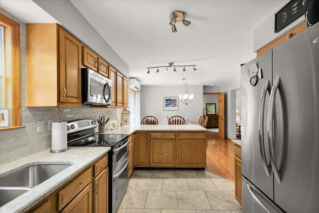 21 Bowling Green Ln, Belfast, ME 04915 - kitchen featuring stainless steel appliances, a peninsula, backsplash, a chandelier, and brown cabinetry