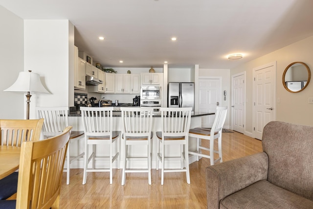 1 E Grand Ave Unit 503, Old Orchard Beach, ME 04064 - kitchen featuring appliances with stainless steel finishes, under cabinet range hood, a peninsula, light wood-style floors, and a breakfast bar area