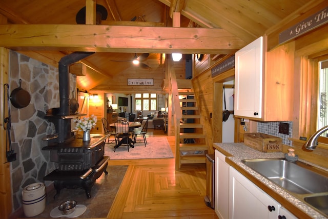 108 Maple Rd, Atkinson, ME 04426 - kitchen featuring a wood stove, white cabinetry, wooden walls, ceiling fan, and open floor plan
