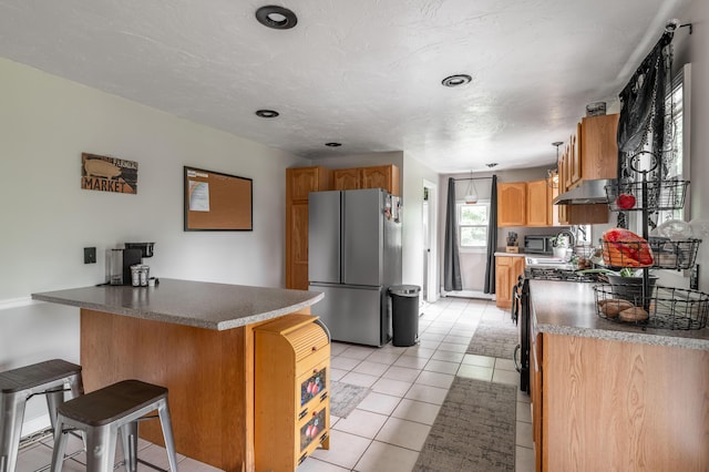 230 W Old Main Rd, Lowell, ME 04493 - kitchen with stainless steel appliances, a breakfast bar, under cabinet range hood, a peninsula, and light tile patterned floors