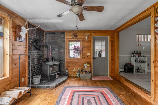 230 W Old Main Rd, Lowell, ME 04493 - foyer featuring hardwood / wood-style flooring, a wood stove, wood walls, a ceiling fan, and a baseboard radiator
