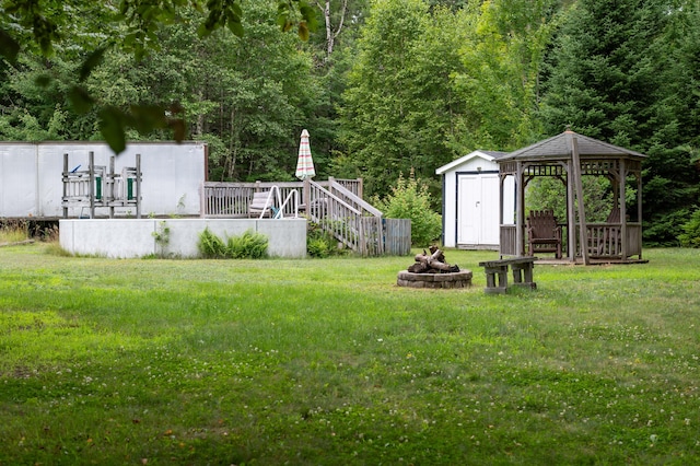 230 W Old Main Rd, Lowell, ME 04493 - view of grassy yard with a fire pit, a shed, a wooden deck, a gazebo, and a forest view