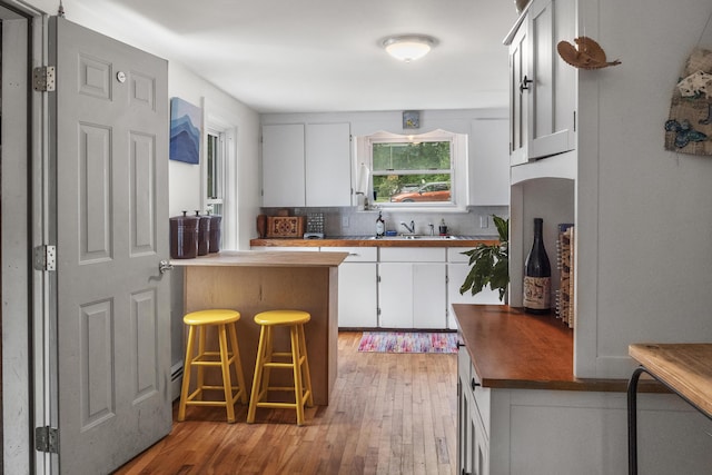 26 Wesley St Ct, Bath, ME 04530 - kitchen featuring light wood-style flooring, tasteful backsplash, white cabinets, a peninsula, and a kitchen breakfast bar