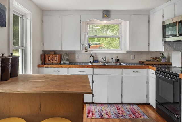 26 Wesley St Ct, Bath, ME 04530 - kitchen featuring black electric range, stainless steel microwave, white cabinets, decorative backsplash, and wood finished floors