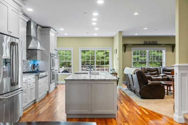 38 Harvest Hill Ln Unit 38, Auburn, ME 04210 - kitchen with stainless steel appliances, wall chimney range hood, light wood finished floors, recessed lighting, and light stone countertops