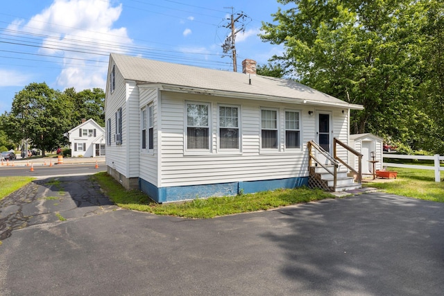 395 Alfred St, Biddeford, ME 04005 - view of front of home with a chimney, entry steps, asphalt driveway, a shed, and roof with shingles