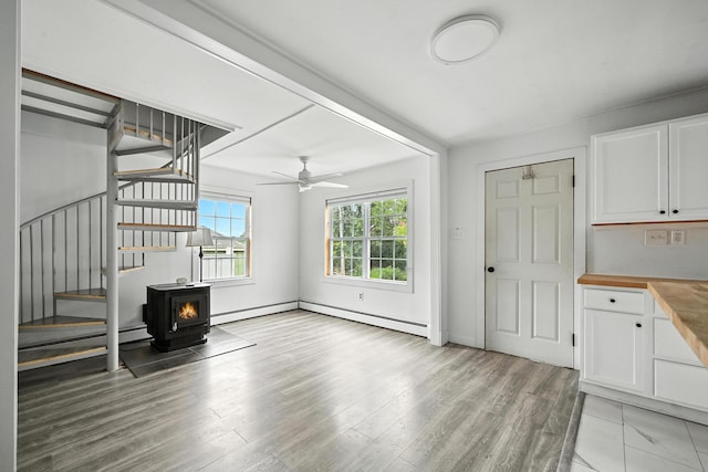 3 Gedney St, Augusta, ME 04330 - unfurnished living room featuring stairs, a ceiling fan, a baseboard heating unit, a wood stove, and light wood finished floors