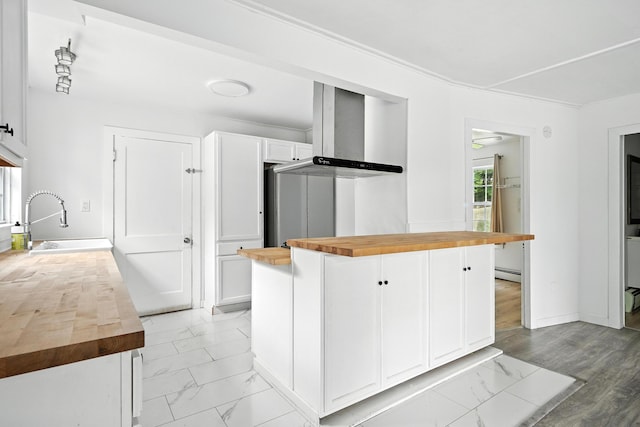 3 Gedney St, Augusta, ME 04330 - kitchen with butcher block countertops, wall chimney range hood, white cabinetry, baseboard heating, and light marble finish floors