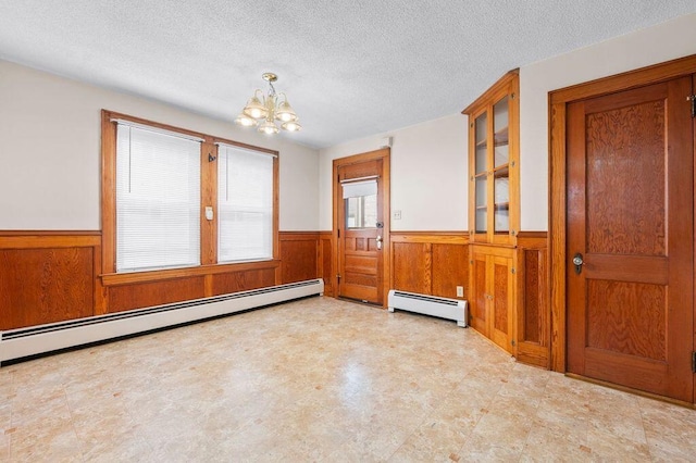 99 Hill St, Biddeford, ME 04005 - spare room with a wainscoted wall, a baseboard heating unit, a chandelier, wood walls, and a textured ceiling