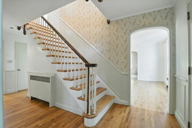 49 Bardwell St, Lewiston, ME 04240 - stairway featuring wallpapered walls, arched walkways, radiator heating unit, wood finished floors, and crown molding