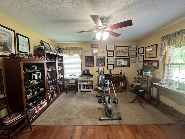 workout area featuring ceiling fan, wood-type flooring, and a textured ceiling