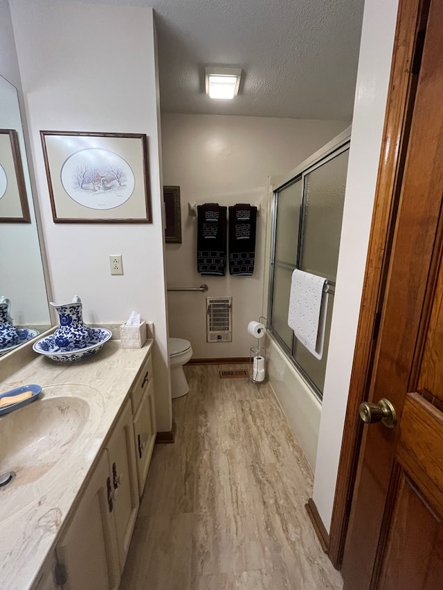 full bathroom with heating unit, wood-type flooring, vanity, toilet, and a textured ceiling