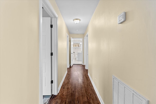 corridor with dark wood-style flooring, visible vents, and baseboards
