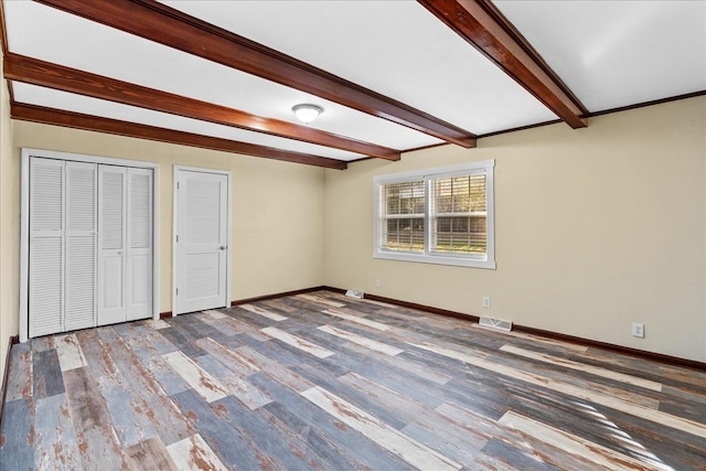 unfurnished bedroom featuring visible vents, baseboards, wood finished floors, beam ceiling, and multiple closets