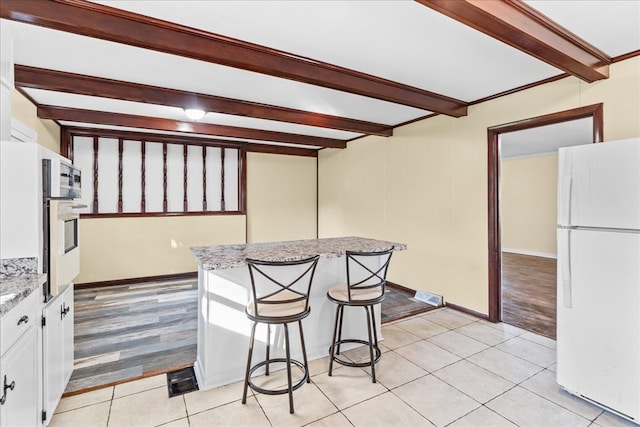 kitchen featuring light tile patterned floors, visible vents, white cabinetry, beam ceiling, and freestanding refrigerator