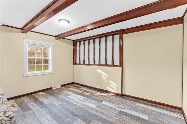 unfurnished room with baseboards, visible vents, wood finished floors, and beamed ceiling