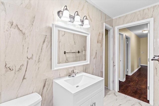 bathroom with toilet, marble finish floor, crown molding, vanity, and tile walls