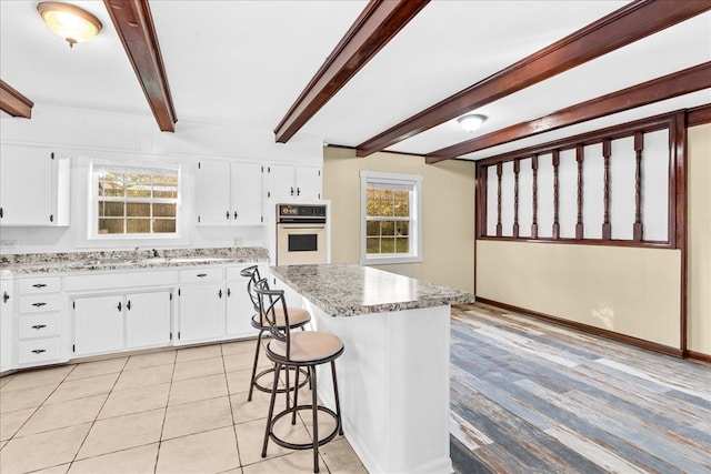 kitchen with white cabinets, a kitchen breakfast bar, a center island, oven, and a sink