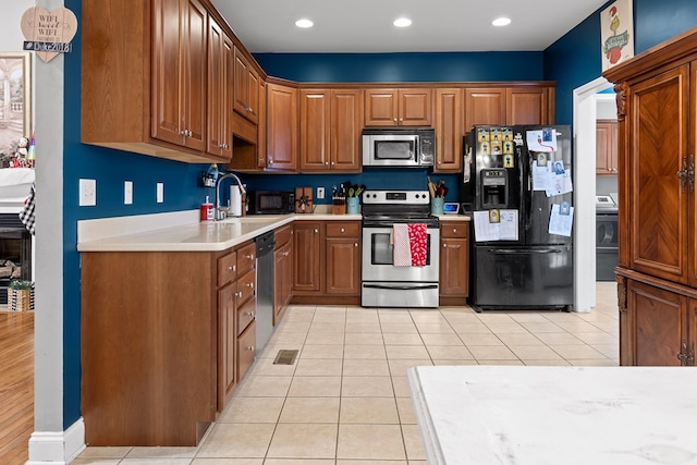 kitchen with light tile patterned flooring, stainless steel appliances, a sink, light countertops, and brown cabinets