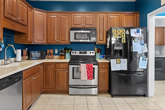 kitchen featuring washer / dryer, brown cabinets, light countertops, black appliances, and a sink