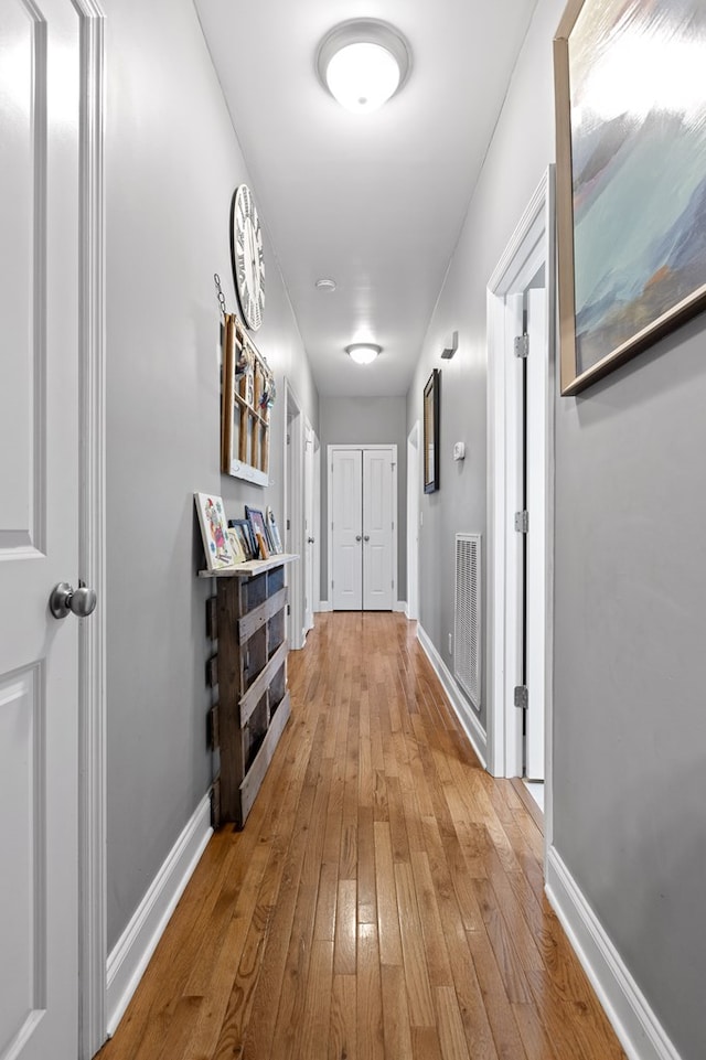 hall with hardwood / wood-style flooring, visible vents, and baseboards