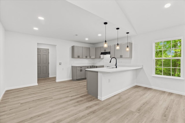 kitchen with a peninsula, baseboards, light countertops, gray cabinets, and under cabinet range hood