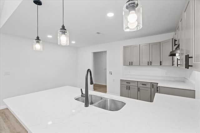 kitchen with light stone counters, a sink, decorative light fixtures, light wood-type flooring, and gray cabinetry