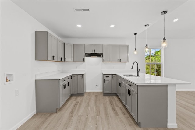 kitchen with a peninsula, a sink, gray cabinets, and light wood finished floors