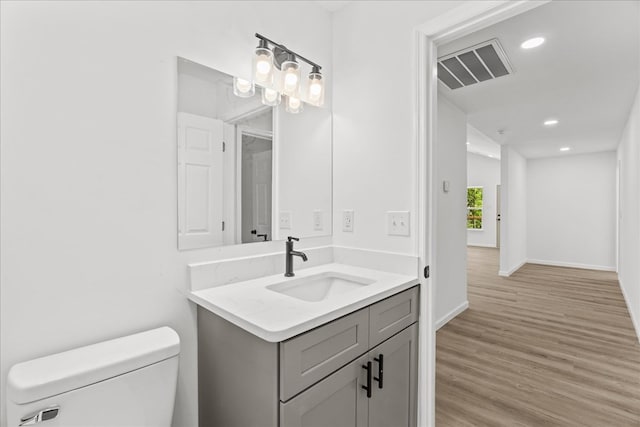 half bath featuring vanity, toilet, baseboards, wood finished floors, and visible vents