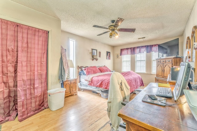 bedroom featuring ceiling fan, visible vents, a textured ceiling, and wood finished floors