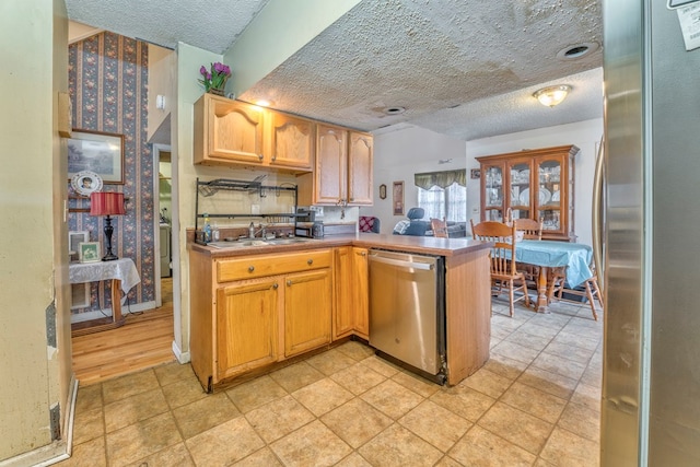 kitchen with light countertops, appliances with stainless steel finishes, a peninsula, a textured ceiling, and a sink