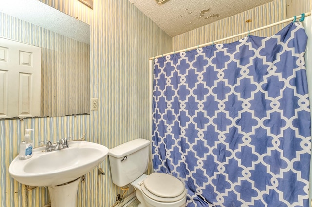 bathroom with toilet, a sink, a textured ceiling, a shower with shower curtain, and wallpapered walls