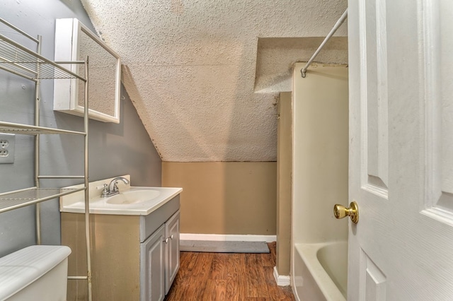 bathroom with toilet, vanity, lofted ceiling, wood finished floors, and a textured ceiling