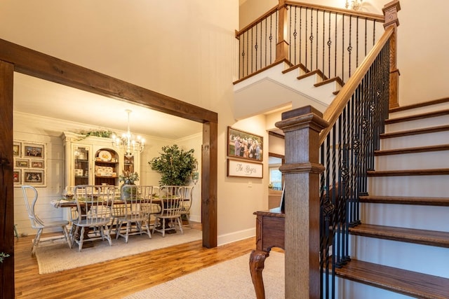 stairway with crown molding, a towering ceiling, a chandelier, and hardwood / wood-style floors