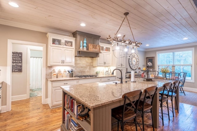 kitchen featuring white cabinetry, hanging light fixtures, tasteful backsplash, light stone countertops, and an island with sink