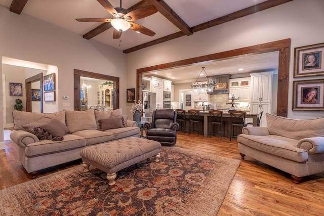 living room featuring beam ceiling, hardwood / wood-style flooring, and ceiling fan with notable chandelier