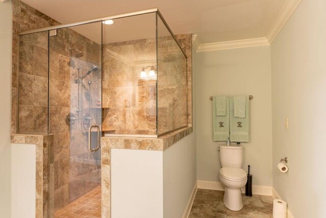 bathroom with ornamental molding, toilet, and a shower with door